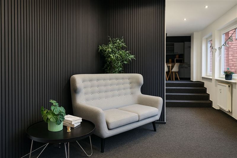 Lounge mit grauem Sofa vor dunkler Lamellenwand, im Hintergrund die Küche